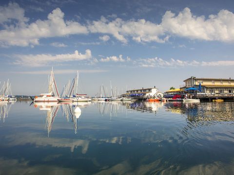 Eine Anlegestelle mit einem Haus und Steg auf der rechten Seite. Links sieht man Segelschiffe und Boote auf dem Wasser des Cospudener Sees.