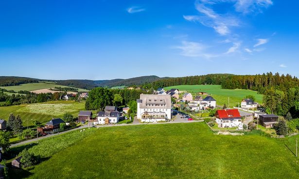 Eine grüne Landschaft mit einigen Häusern und den Wohlfühlbergen in Markneukirchen im Vogtland. 