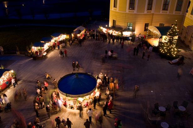 Small stands, a small stage and a Christmas tree are set up in front of Moritzburg Castle. There is a lot of activity in the evening Advent atmosphere.