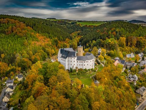 In der Mitte des Bildes ist die Burg Scharfenstein von oben zu sehen. Rundherum befinden sich Bäume und Häuser.