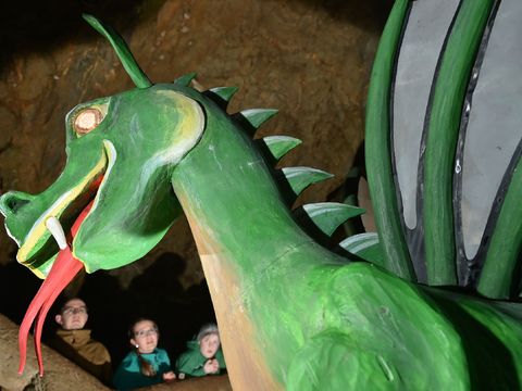 Ein grüner Drache bei der Drachenhöhle Syrau im Vogtland steckt seine rote Zunge heraus. Im Hintergrund sind Kinder.